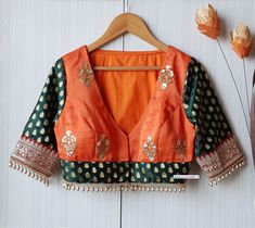 This Made to Order/Made to Measurement/Custom Made Indian Ethnic Blouse. - Fabric - Embroidered Upada Silk and Brocade - Color - Orange and Green - Padded - Deep V  Front Neck; Back Closed - Front Hook Closure  - Fringes around the waist and sleeves - Elbow length Brocade Sleeves with Border - Rich Lining - Princess Cut PLEASE NOTE: BUYERS ARE RESPONSIBLE FOR ANY CUSTOMS AND IMPORT TAXES THAT MAY APPLY. This is a made to order product. If you opt for 'Made To Measurement Option', we will provide Green V-neck Choli For Festive Occasions, Festive Green V-neck Choli, Bohemian Art Silk Blouse With Motifs, Fitted Bohemian Art Silk Blouse, Bohemian Art Silk Fitted Blouse, Deep V Neck Blouse Indian, Closed Neck Blouse Designs, Front V Neck Blouse Designs, Orange Blouse Designs