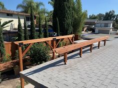 a long wooden bench sitting on top of a brick walkway next to trees and bushes