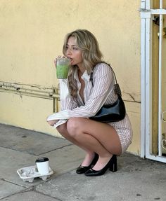 a woman sitting on the ground drinking from a green cup while holding a black purse