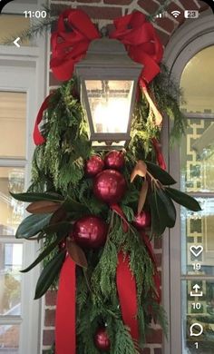 a christmas wreath with red balls and greenery hanging from the side of a building