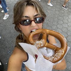 a woman wearing sunglasses and eating a giant pretzel