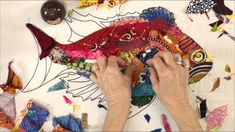 a person is working on a fish made out of fabric and paper with colored threads