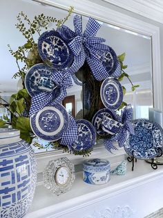 blue and white dishes are arranged in front of a wreath on a mantle with greenery