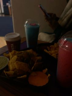 a tray full of food and drinks on a table next to a person holding a cell phone