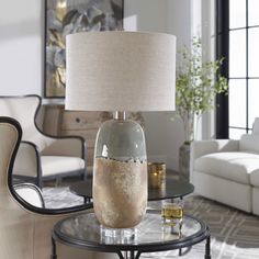 a glass table with a lamp on it in front of a white couch and chair