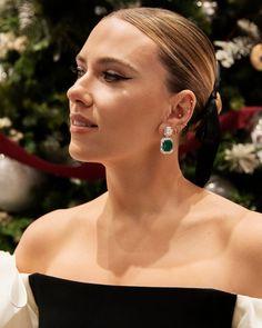 a woman in a black and white dress with green earrings on her left ear, looking off to the side