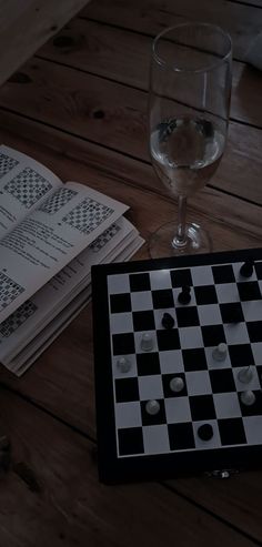 a glass of wine sitting on top of a wooden table next to a chess board