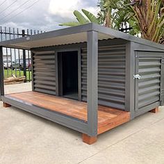 a small gray building sitting on top of a wooden platform next to a palm tree