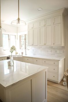 a large kitchen with white cabinets and an island in the middle is shown, along with a vase filled with flowers