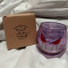 a purple glass cup with an evil face on it next to a box that says pokemon cafe