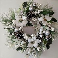 a wreath with white flowers, pine cones and silver baubs is hanging on the wall