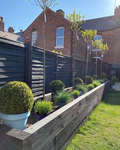 a wooden planter filled with potted plants next to a fenced in yard