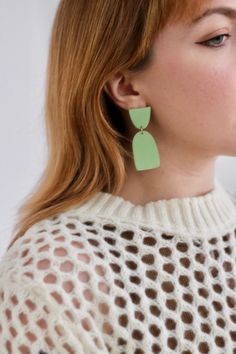 a woman with red hair wearing green earrings and a white sweater is looking off to the side