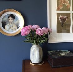 a vase filled with pink flowers sitting on top of a wooden table next to a framed photo