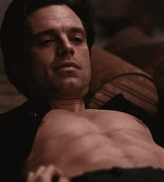 a shirtless man laying on a couch looking off to the side with his eyes closed