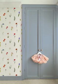 an open closet door with a pink dress hanging from it's side in front of a floral wallpaper