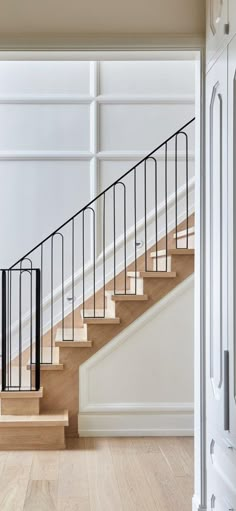 an open door leading to a stair case in a white room with wood floors and walls