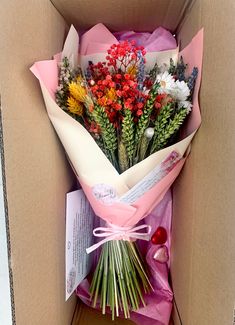 a bouquet of flowers is wrapped in pink tissue paper and placed inside a cardboard box