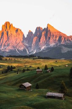 the mountains are covered in snow and green grass, with small cabins nestled at the base