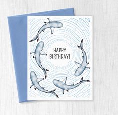 a birthday card with dolphins swimming in a circle on top of a blue envelope that says happy birthday