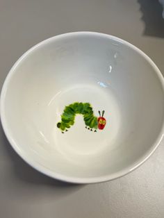 a white bowl with a green and red caterpillar painted on it's side