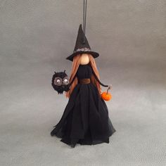 a doll dressed as a witch holding a pumpkin and a black cat hanging from a hook