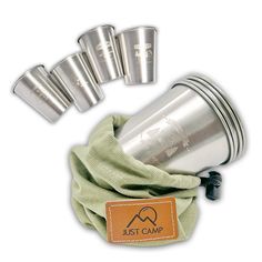 a set of four stainless steel cups sitting on top of a green cloth next to it's holder