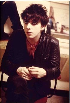 a young man sitting in a chair with his hands on his knees and looking at the camera