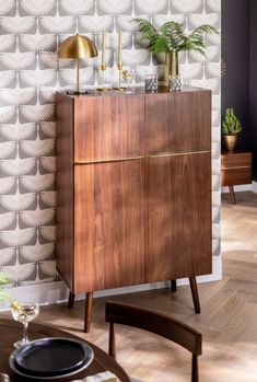 a wooden cabinet sitting in front of a wallpapered wall with plants on it