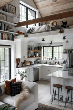 a living room filled with furniture and lots of books on top of the shelves next to a kitchen