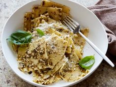 a white bowl filled with pasta covered in pesto and parmesan cheese next to a fork