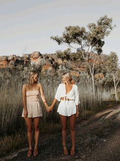 two women holding hands walking down a dirt road