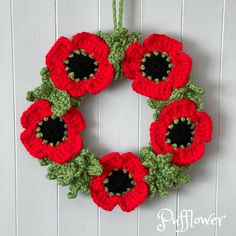 a crocheted wreath with red flowers hanging on a white wooden wall next to a pair of scissors