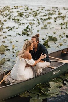 a man and woman sitting in a boat on the water with lily pads around them