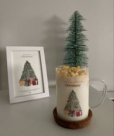 a glass mug filled with peanuts and a christmas tree on top of it next to a framed photo