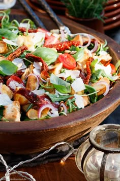 a wooden bowl filled with lots of salad on top of a table next to silverware