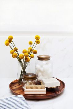 a wooden tray topped with yellow flowers next to a jar filled with soap and other items