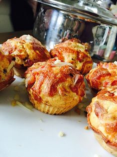 several mini pizzas on a white plate next to a silver pot and utensil