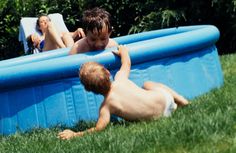 two young boys playing in an inflatable pool on the grass with their parents