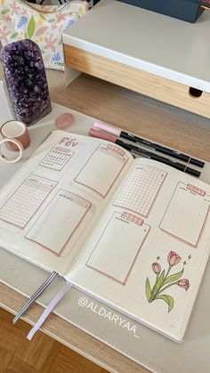 an open planner book sitting on top of a table next to a vase with flowers