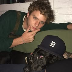 a man laying on top of a couch next to a black dog wearing a hat