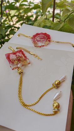 two pieces of jewelry sitting on top of a piece of paper next to some plants