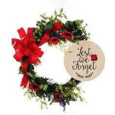 a wreath with red flowers and greenery is hanging on a white wall next to a sign that says, let me forget