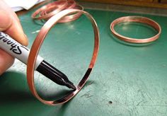 a hand holding a marker near a pair of copper colored metal bracelets on a green surface