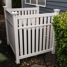 a white fence in front of a blue house with bushes and shrubbery next to it