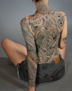 a woman sitting on the floor with tattoos on her back and arms behind her head