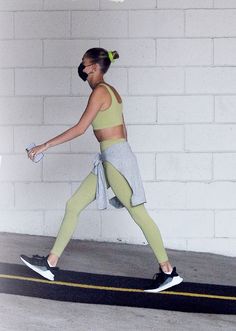 a woman in yellow sports bra top and leggings walking down the street with her tennis racket