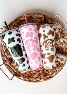 three starbucks cups with different designs on them sitting in a wicker basket next to a cell phone