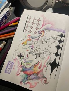 a drawing with colored pencils and headphones on a desk next to some books