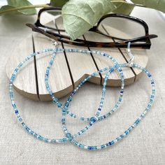 Dainty and bohemian eyeglass necklace chain made with tiny Preciosa Czech crystal seed beads in blue tones and small round faceted cubic zirconia crystals.   Paired with beautiful blue cz gems, this handmade eyeglass chain will definitely create a unique look. This eyeglass lanyard is made on strong quality beading wire with silver plated wire guardians that protect the eyeglass holder grips. The necklace is ended with spring clasps that hold the eyeglass grips and they can be easily removed to Adjustable Glass Necklaces With Tiny Beads, Beaded Clear Glass Glasses Chains, Adjustable Glass Necklace With Tiny Beads, Glass Bead Necklaces For Beach, Glass Necklaces With Tiny Beads For The Beach, Clear Beaded Glass Glasses Chains, Glass Tiny Beads Necklace For Beach, Adjustable Glass Beaded Necklaces With Tiny Beads, Handmade Adjustable Blue Glasses Chains